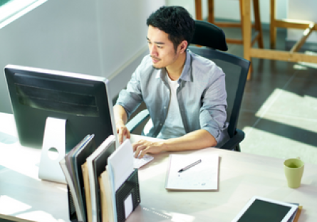 a man using a laptop sitting a brightly lit cubicle
