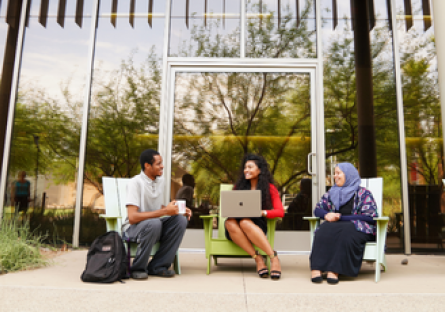 Three students sitting outside working on their laptops