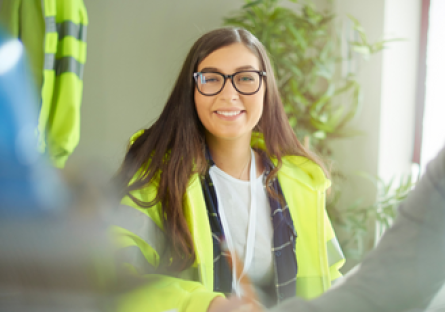 Image of a female construction worker how appears in focus with a male construction in the foreground 