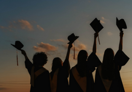 Image of four graduating students raising their caps in the air.