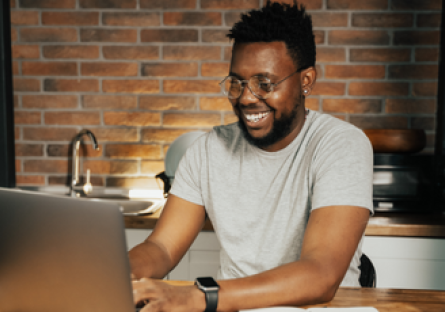 A man wearing a grey T-shirt working on a laptop