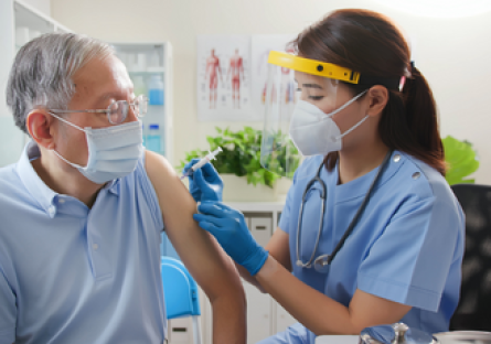 Image of a woman healthcare professional wearing PPE giving a vaccine to a elderly man