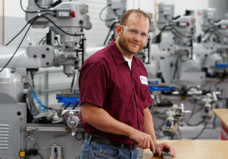 Image of a man wearing a maroon shirt smiling with machinery in the background