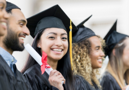 A group of college graduates wearing caps and gowns and one woman holding a diploma and smiling