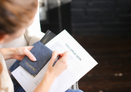 An image of a woman holding a passport and completing Visa form