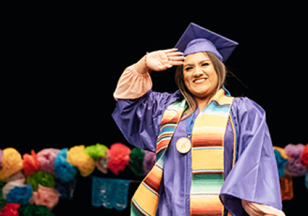 An image of a female student wearing a graduation cap, gown, and colorful stole attending a Hispanic Convocation Ceremony