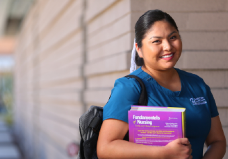 An image of a smiling woman wearing nursing scrubs and holding nursing textbooks
