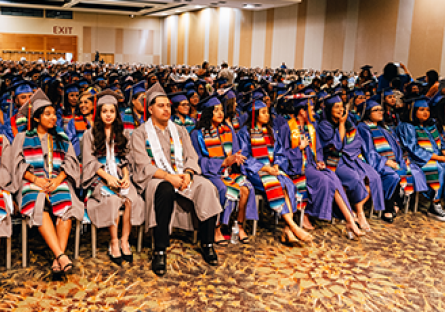 Room of students wearing cap and gowns during graduation ceremony.